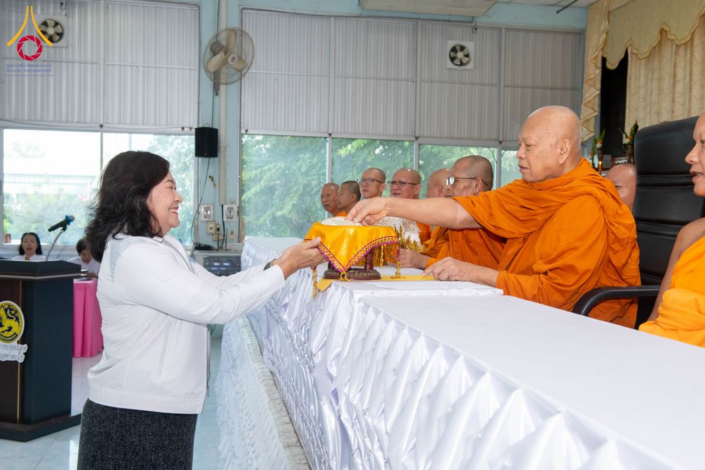 หญิงสวมเสื้อสีขาวกำลังประเคนสิ่งของบนพานทองแด่พระภิกษุสงฆ์
