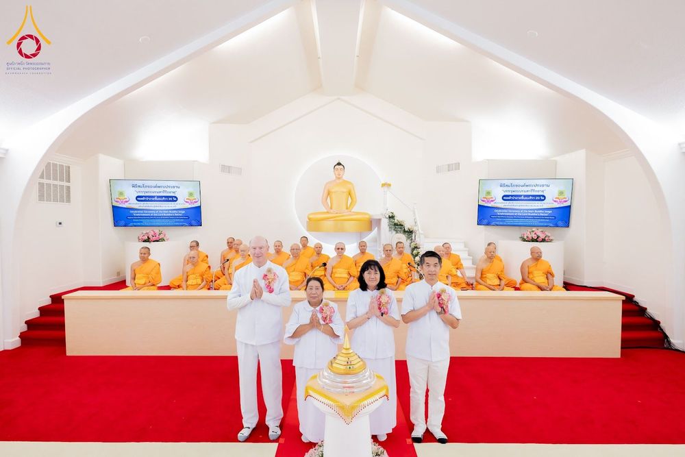 กลุ่มพระภิกษุสงฆ์และพุทธศาสนิกชนในชุดขาวร่วมพิธีทางศาสนาหน้าพระพุทธรูปภายในวัด