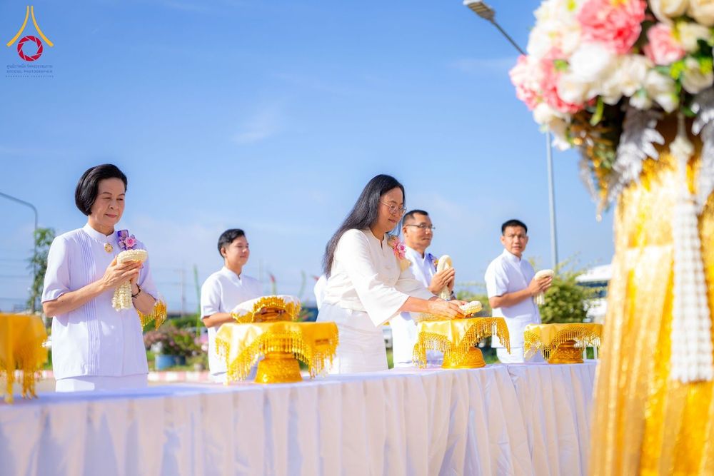กลุ่มคนในชุดขาวกำลังวางพวงมาลัยบนพานทองในพิธีทางศาสนากลางแจ้ง