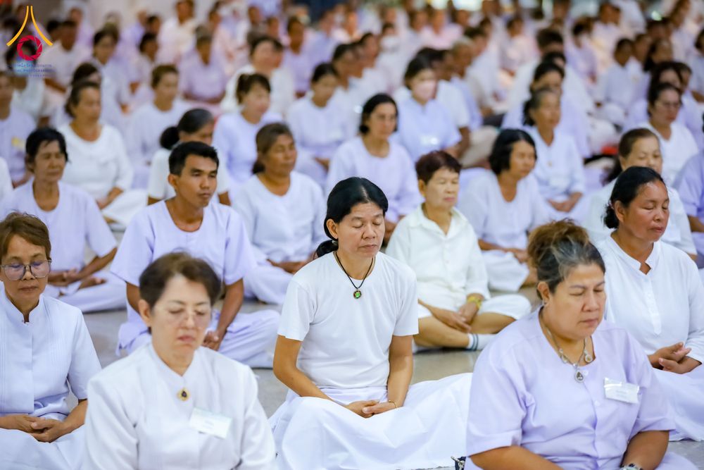 กลุ่มคนสวมชุดขาวนั่งสมาธิเรียงแถวกันอย่างเป็นระเบียบภายในห้องโถง