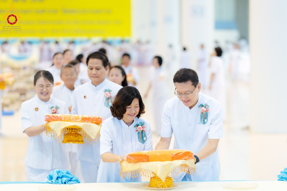 กลุ่มคนสวมชุดสีขาวกำลังถือพานพุ่มผ้าไตรจีวรในพิธีทางศาสนา