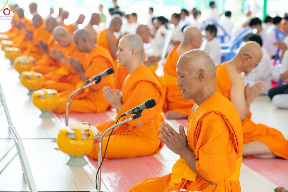 พระภิกษุและนาคหลายรูปนั่งพนมมือในพิธีอุปสมบทหมู่