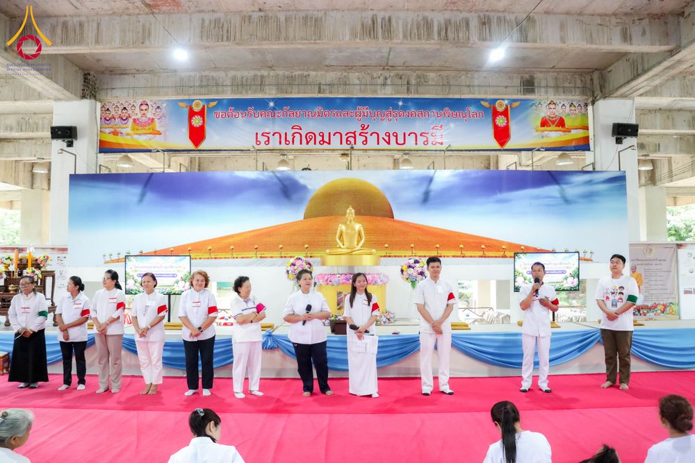 กลุ่มผู้เข้าร่วมโครงการสวมชุดสีขาวกำลังยืนบนเวทีที่มีฉากหลังเป็นป้ายข้อความและภาพพระพุทธรูป