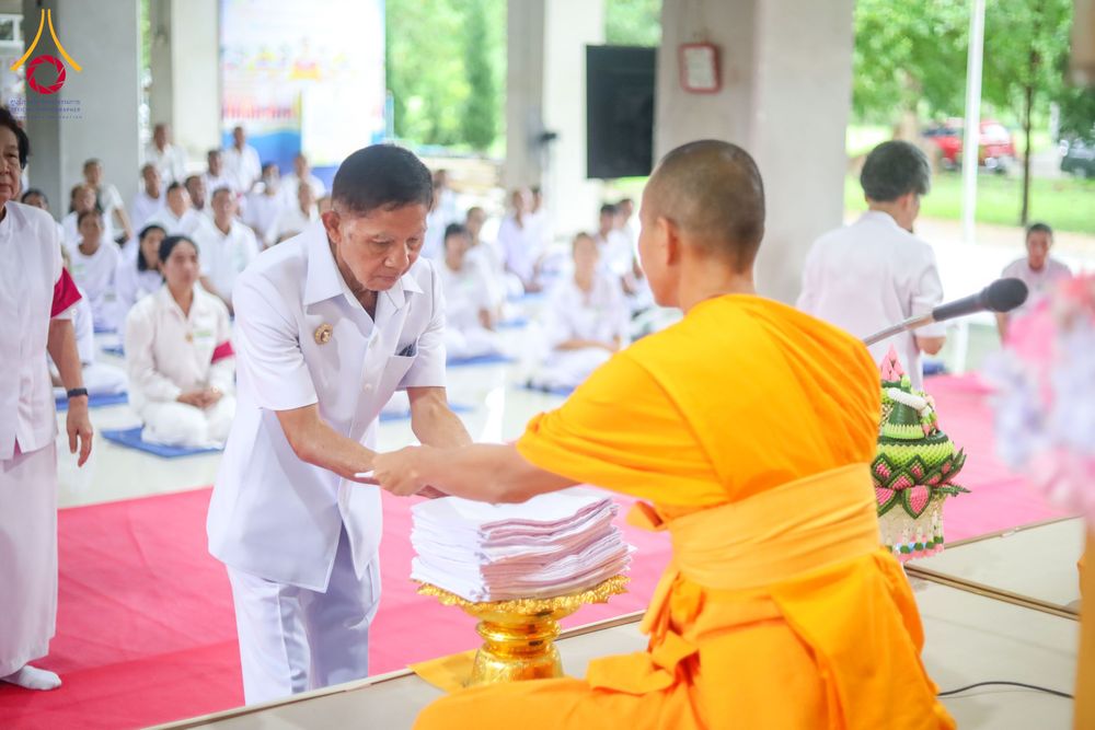 ชายในชุดขาวกำลังประเคนผ้าไตรแด่พระภิกษุสงฆ์ในพิธีทางศาสนา