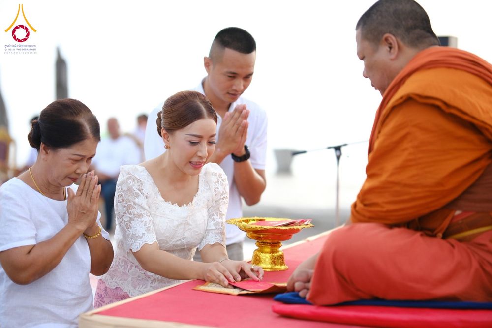 หญิงสาวกำลังถวายปัจจัยแด่พระภิกษุสงฆ์ในพิธีตักบาตร โดยมีผู้ร่วมงานพนมมืออยู่ด้านข้าง