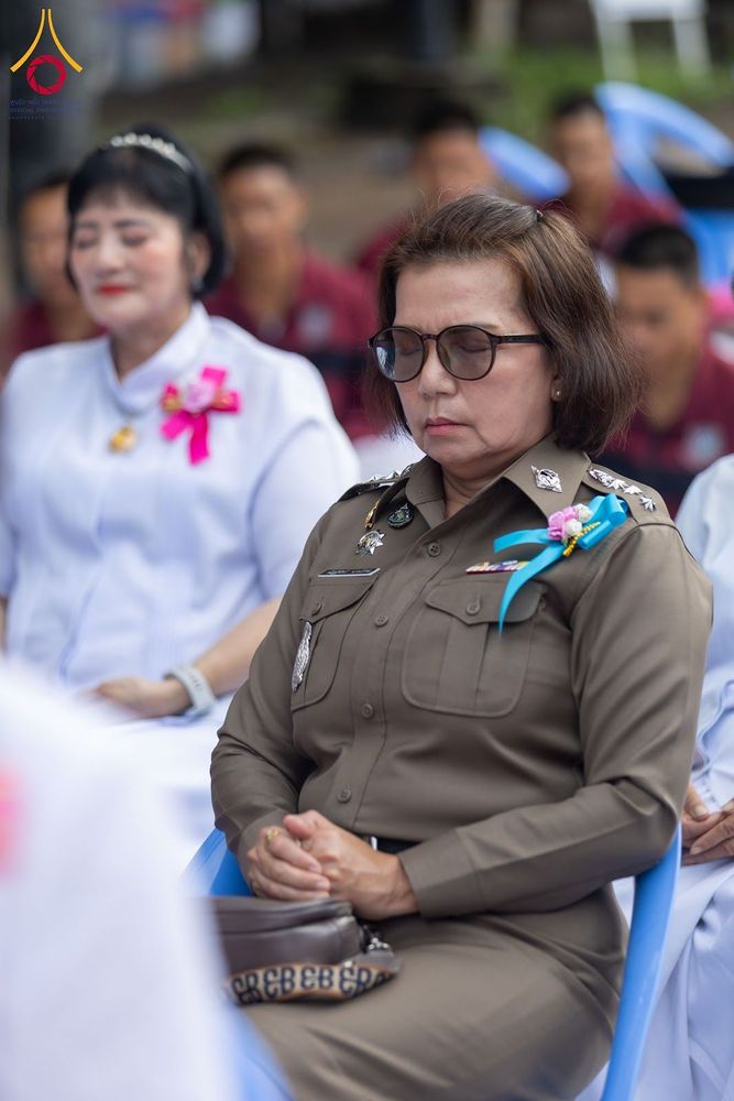เจ้าหน้าที่ตำรวจหญิงสวมแว่นตานั่งหลับตาทำสมาธิร่วมกับผู้เข้าร่วมพิธีคนอื่น ๆ