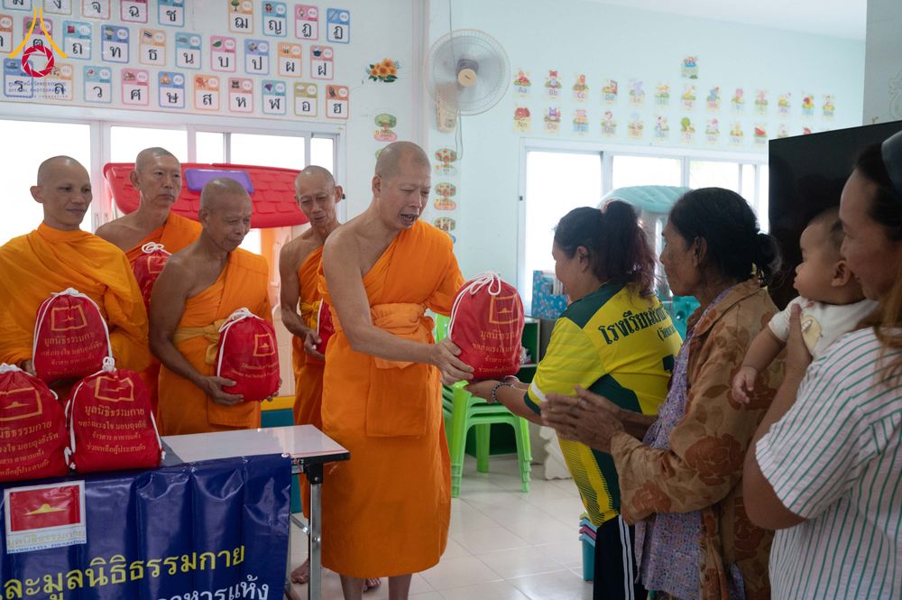 พระสงฆ์ในจีวรสีส้มกำลังส่งมอบถุงยังชีพสีแดงให้แก่ชาวบ้านที่มารับความช่วยเหลือ
