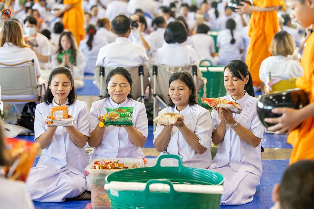 กลุ่มผู้หญิงสวมชุดขาวถืออาหารแห้งเตรียมตักบาตรพระสงฆ์ในพิธีทางศาสนา
