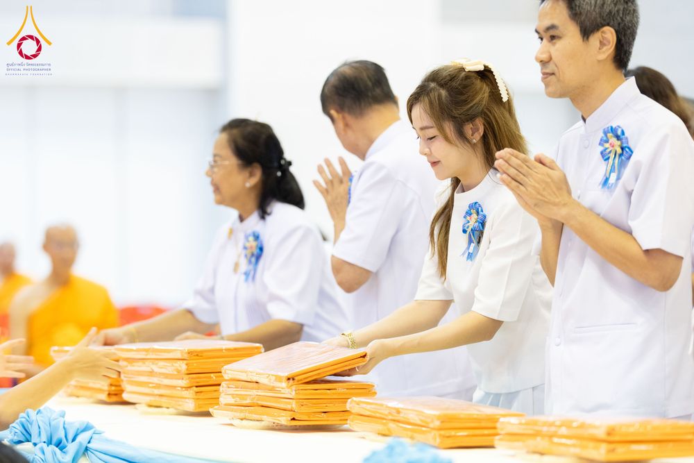 กลุ่มคนสวมชุดขาวกำลังส่งมอบผ้าไตรจีวรในพิธีทางศาสนา