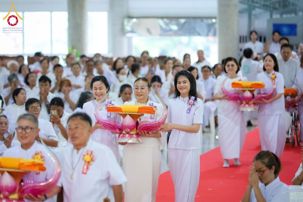 กลุ่มพุทธศาสนิกชนแต่งกายชุดสีขาวถือพานพุ่มผ้าไตรเดินแถวในอาคาร