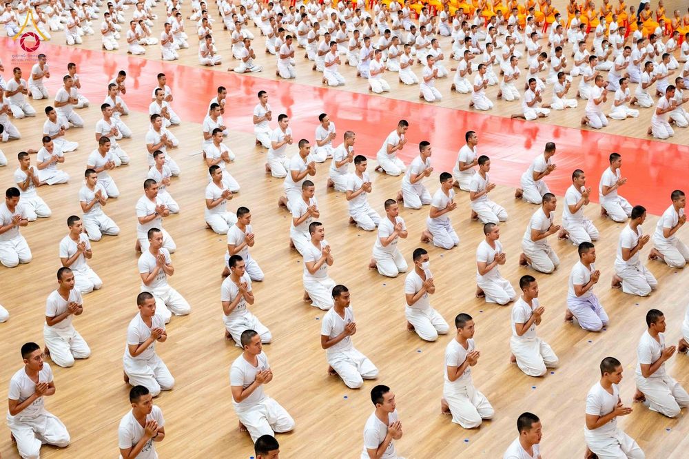 นักเรียนนายสิบตำรวจจำนวนมากในชุดขาวนั่งพนมมือบนพื้นไม้ภายในอาคาร