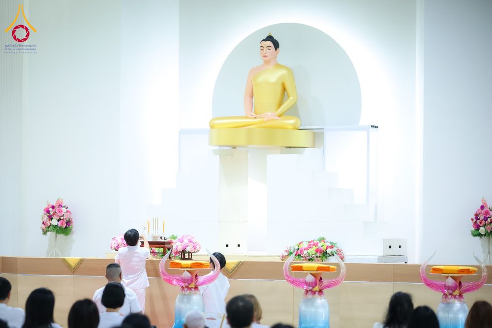 พุทธศาสนิกชนในชุดขาวประกอบพิธีหน้าองค์พระพุทธรูปสีทองภายในอาคาร