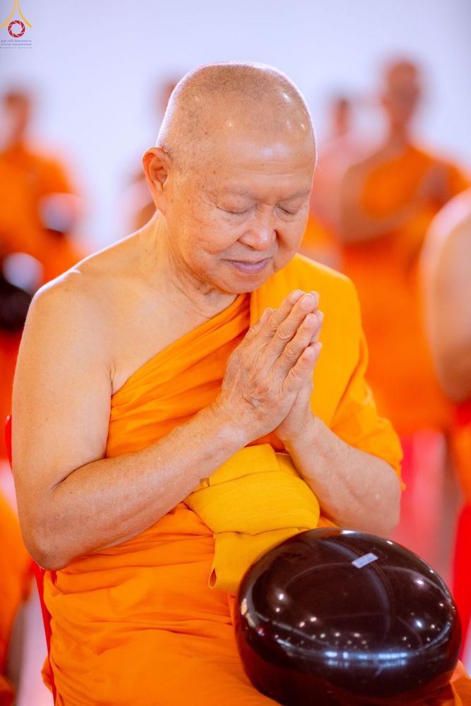 พระภิกษุสงฆ์ครองจีวรสีส้มกำลังประนมมือไหว้และมีบาตรวางอยู่ด้านหน้า