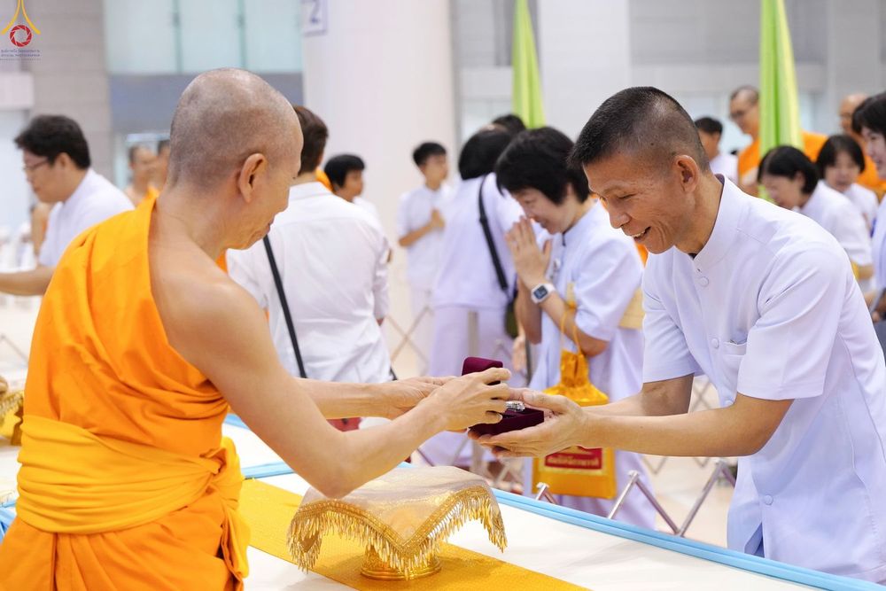 พระภิกษุกำลังมอบกล่องพระของขวัญให้แก่ชายในชุดสีขาวภายในห้องโถง
