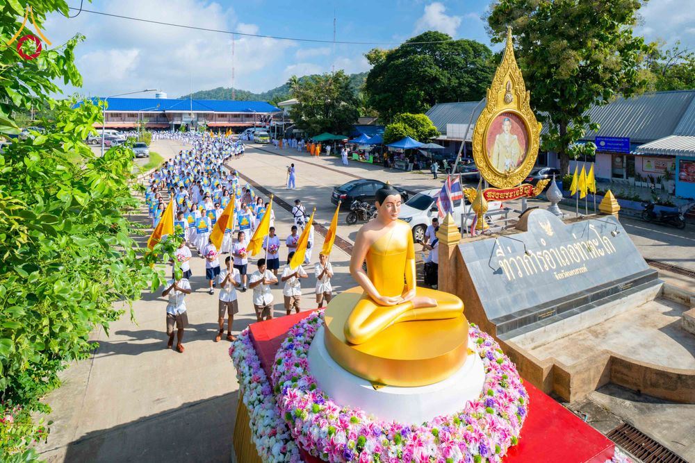 ขบวนพุทธศาสนิกชนเดินแถวตามรถบุษบกที่ประดิษฐานพระพุทธรูปสีทองผ่านหน้าป้ายที่ว่าการอำเภอท่าตะโก
