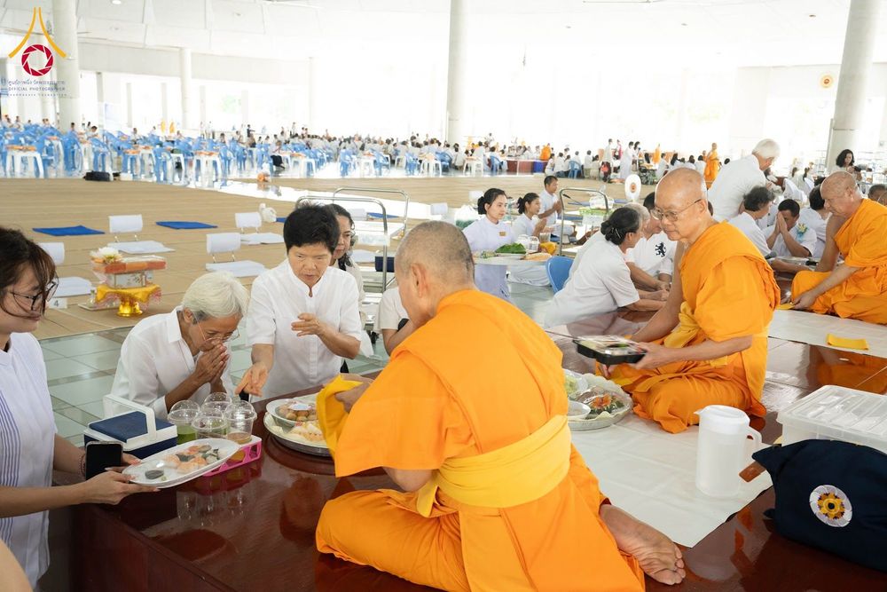 พระภิกษุสงฆ์และพุทธศาสนิกชนในชุดขาวกำลังประกอบพิธีถวายภัตตาหารภายในอาคารหอฉัน