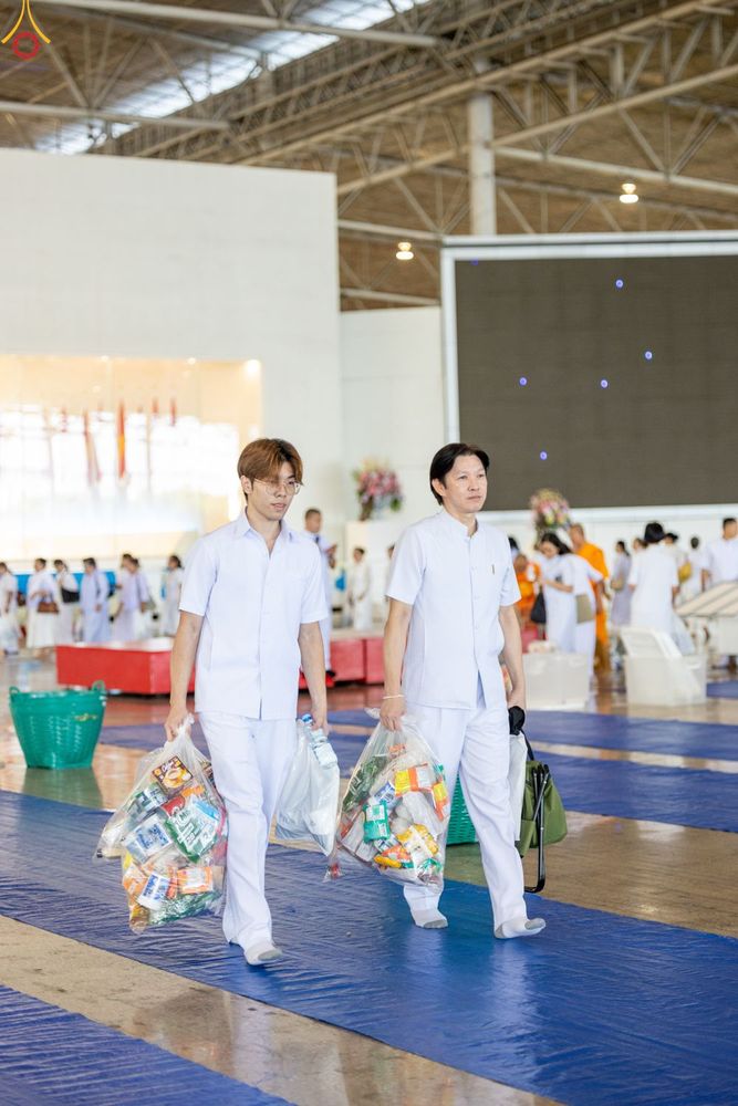 ชายสองคนสวมชุดสีขาวถือถุงใส่ของแห้งเดินภายในสภาธรรมกายสากล