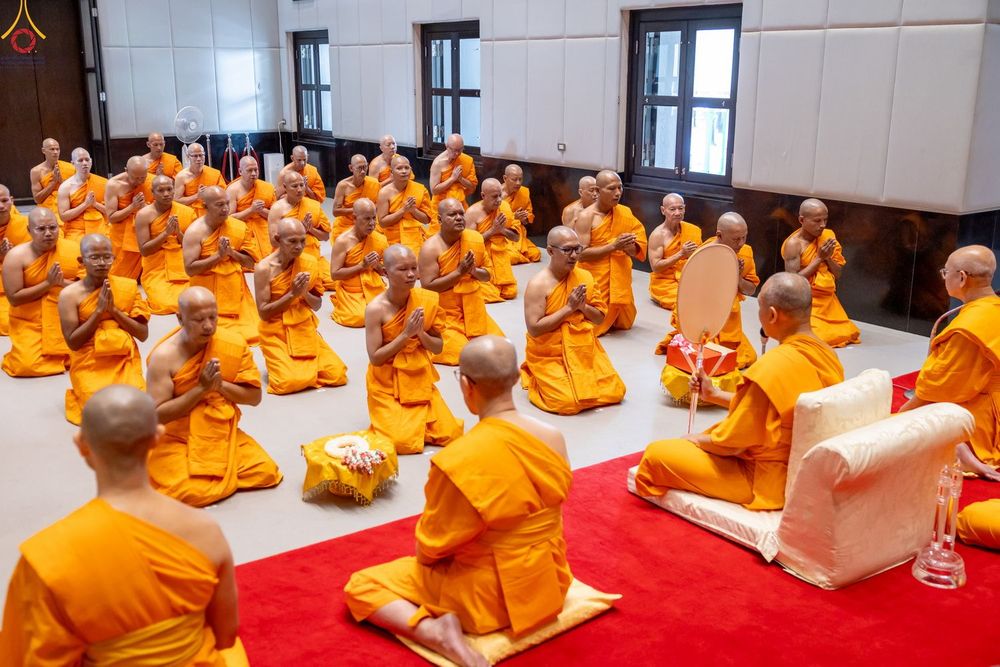 พระภิกษุและสามเณรจำนวนมากนั่งพนมมือประกอบพิธีทางศาสนาภายในอาคาร