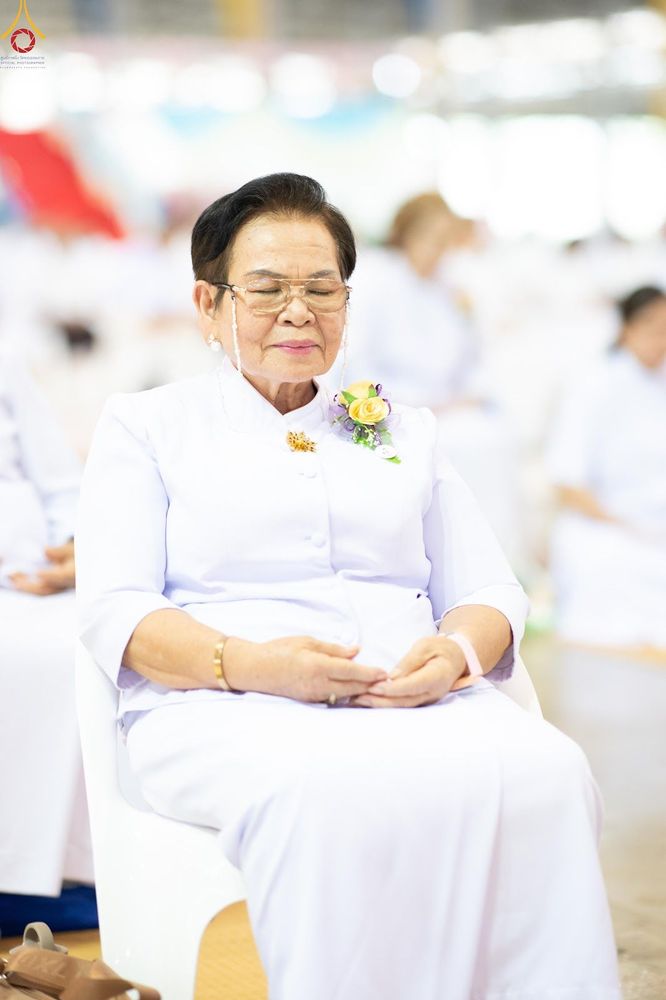 หญิงสูงวัยสวมชุดขาวนั่งหลับตาทำสมาธิในพิธีทางศาสนา