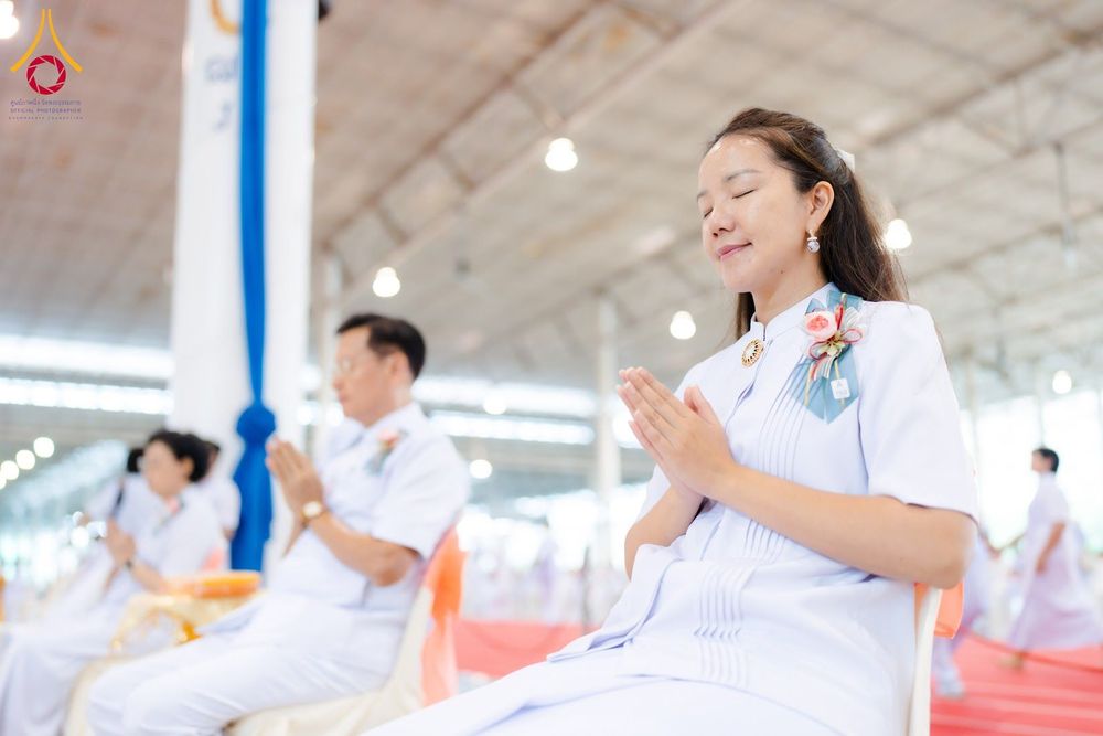 หญิงสาวสวมชุดสีขาวนั่งพนมมือหลับตาด้วยความสงบในพิธีทางศาสนา