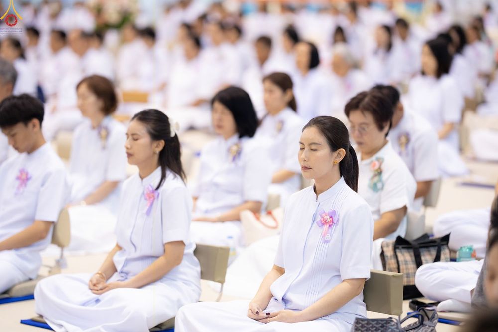 กลุ่มคนสวมชุดขาวนั่งหลับตาสมาธิภายในหอประชุมขนาดใหญ่