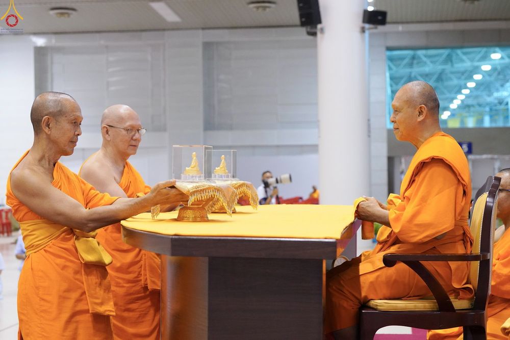 พระภิกษุสงฆ์ในจีวรสีส้มกำลังทำพิธีมอบพระของขวัญสีทองบนโต๊ะ