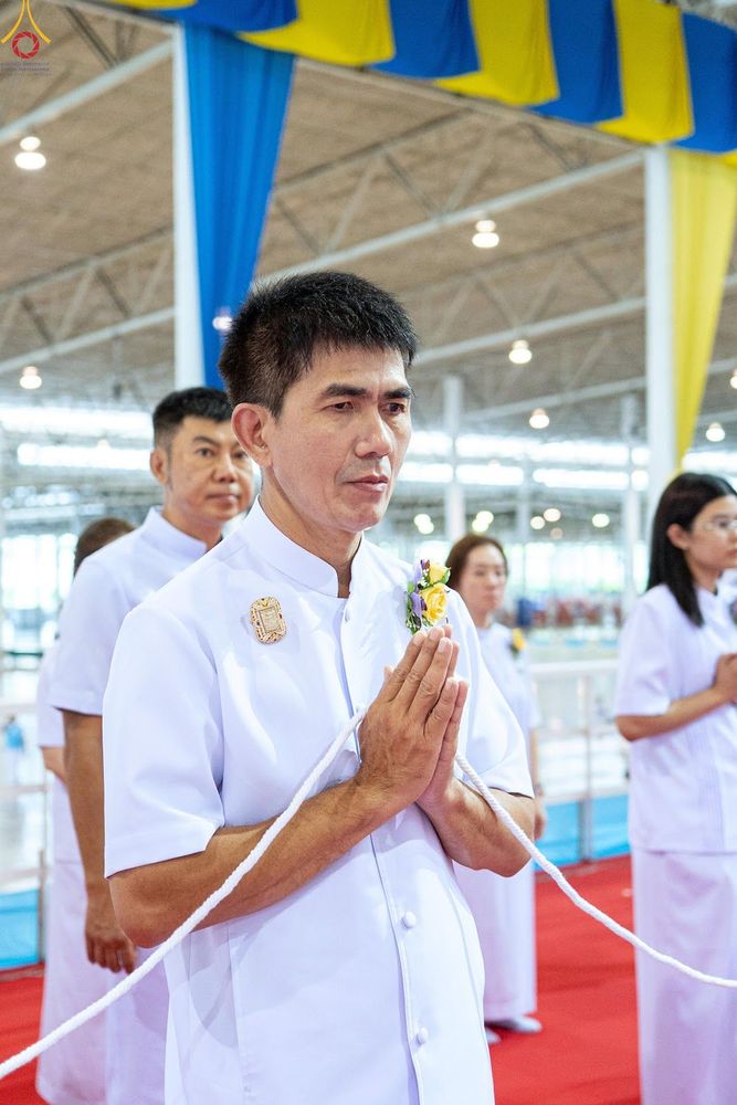 ชายและหญิงสวมชุดสีขาวกำลังยืนพนมมือถือสายสิญจน์ในพิธีทางศาสนา