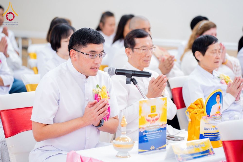 กลุ่มพุทธศาสนิกชนสวมชุดขาวนั่งพนมมือร่วมพิธีทอดผ้าป่าภายในอาคาร