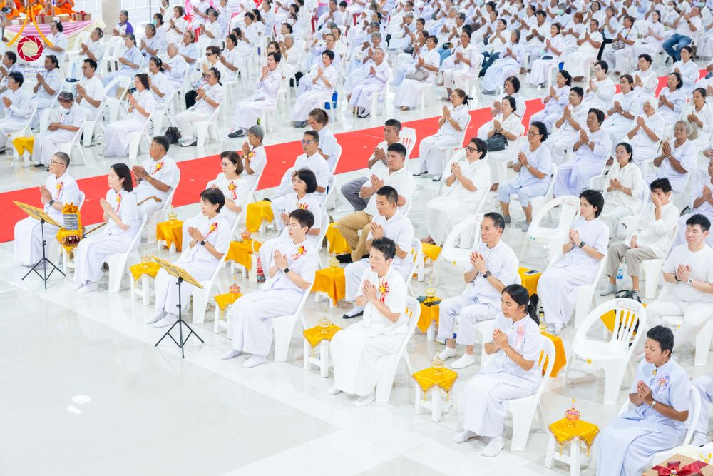 พุทธศาสนิกชนสวมชุดขาวนั่งพนมมือร่วมพิธีทางศาสนาภายในอาคาร