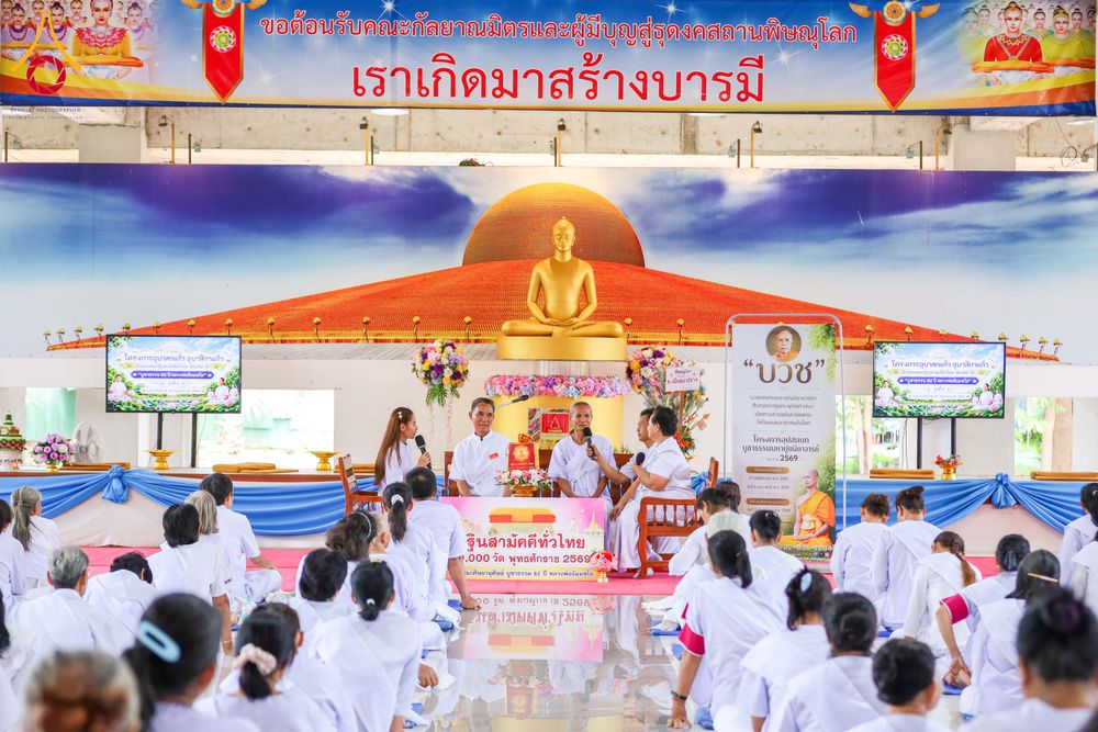 กลุ่มผู้เข้าร่วมโครงการสวมชุดขาวนั่งฟังการบรรยายธรรมภายในอาคารที่มีป้ายโครงการและพระพุทธรูปเป็นฉากหลัง