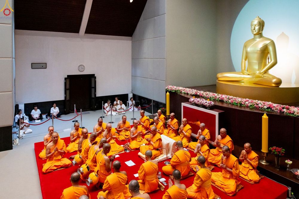 พระภิกษุและสามเณรจำนวนมากนั่งประกอบพิธีกรรมทางศาสนาภายในโบสถ์ที่มีพระพุทธรูปสีทองประดิษฐานอยู่