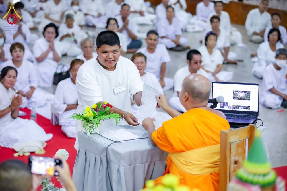 ชายหนุ่มยื่นเอกสารให้พระภิกษุสงฆ์ท่ามกลางผู้เข้าร่วมโครงการสวมชุดขาว