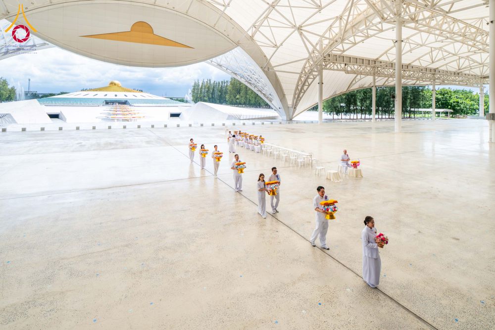 กลุ่มคนชุดขาวถือพานดอกไม้เดินเป็นแถวภายในอาคารสภาธรรมกายสากล