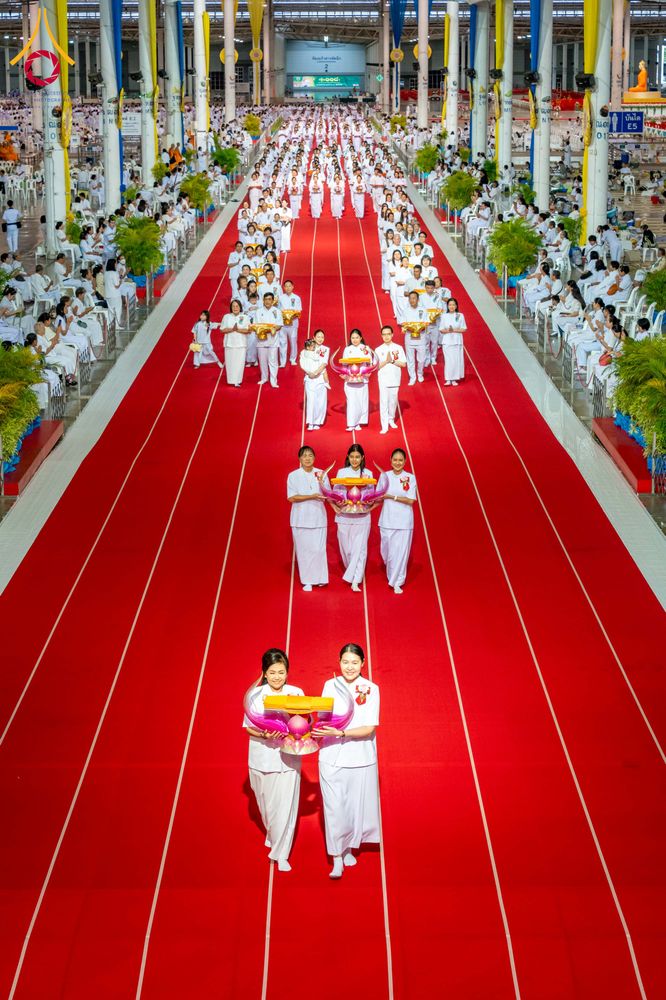 กลุ่มคนชุดขาวถือพานพุ่มเดินบนพรมแดงในอาคารสภาธรรมกายสากล