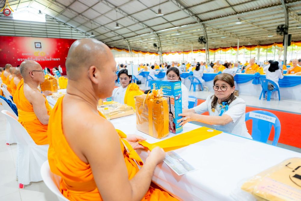 หญิงสวมเสื้อสีขาวกำลังส่งมอบชุดสังฆทานให้กับพระภิกษุในงานบุญ