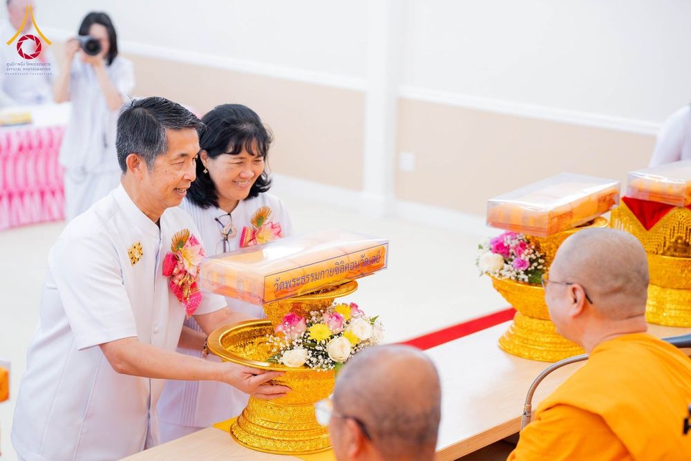 ชายและหญิงสวมชุดสีขาวกำลังประเคนพานผ้าป่าสีทองแด่พระภิกษุสงฆ์ในพิธีทำบุญ