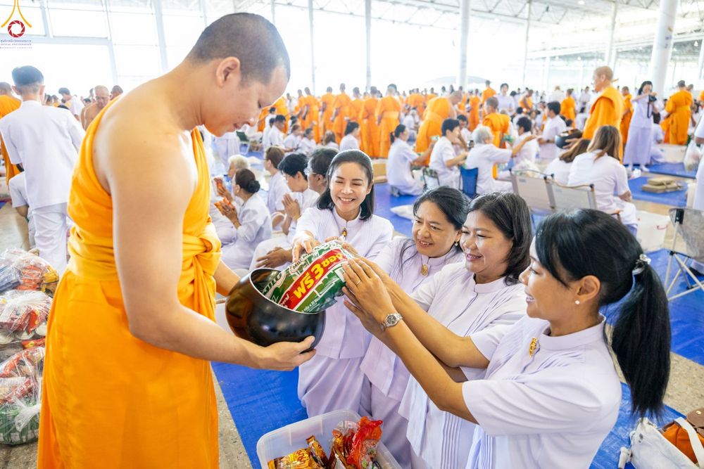พุทธศาสนิกชนชุดขาวกำลังใส่บาตรข้าวสารอาหารแห้งแด่พระภิกษุสงฆ์ในพิธีตักบาตร