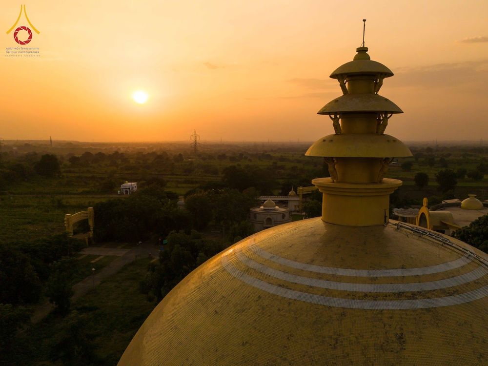 ยอดเจดีย์สีทองทรงกลมและฉัตรด้านบน ตัดกับแสงสีส้มของพระอาทิตย์ตกดินเหนือทัศนียภาพพื้นที่กว้าง