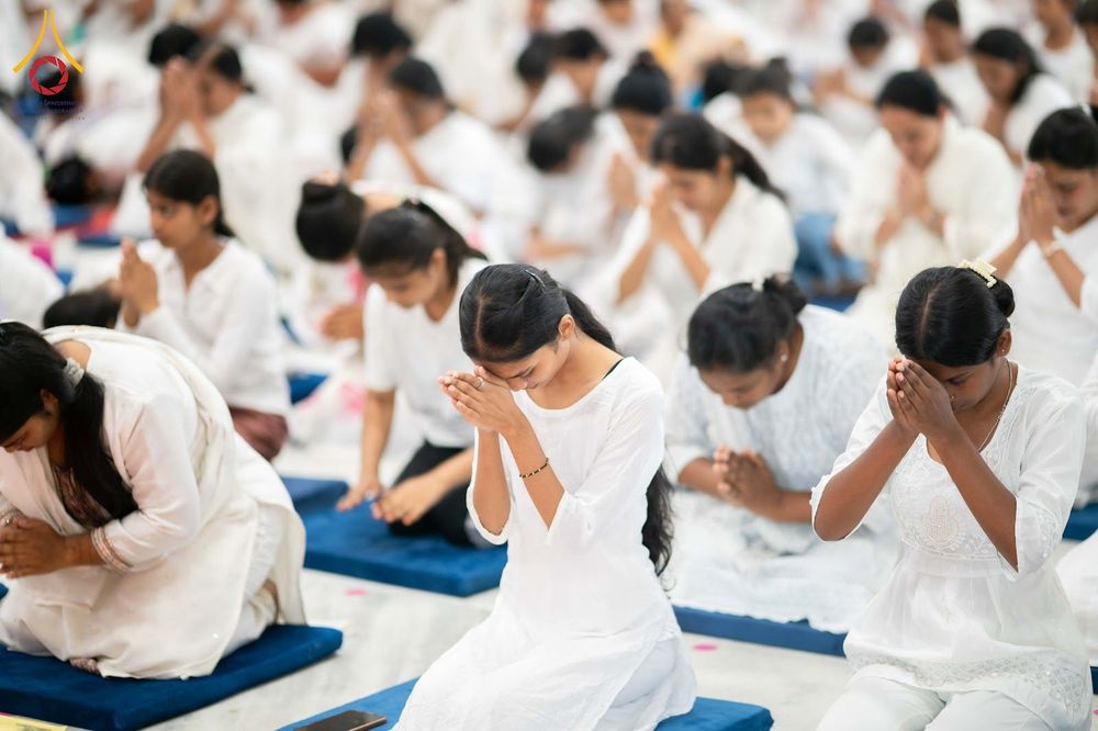 กลุ่มคนสวมชุดสีขาวนั่งพนมมือปฏิบัติธรรมบนเบาะรองนั่งสีน้ำเงิน
