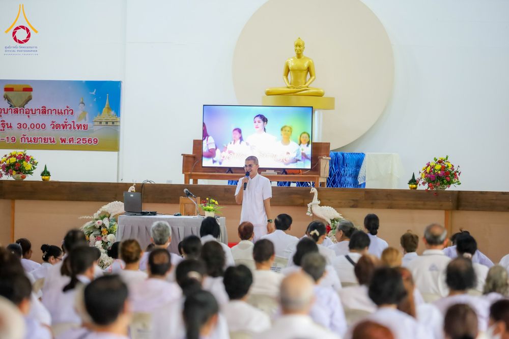 วิทยากรชายสวมชุดขาวกำลังบรรยายธรรมให้แก่ผู้เข้าร่วมโครงการที่สวมชุดขาวนั่งฟังอยู่ภายในหอประชุม