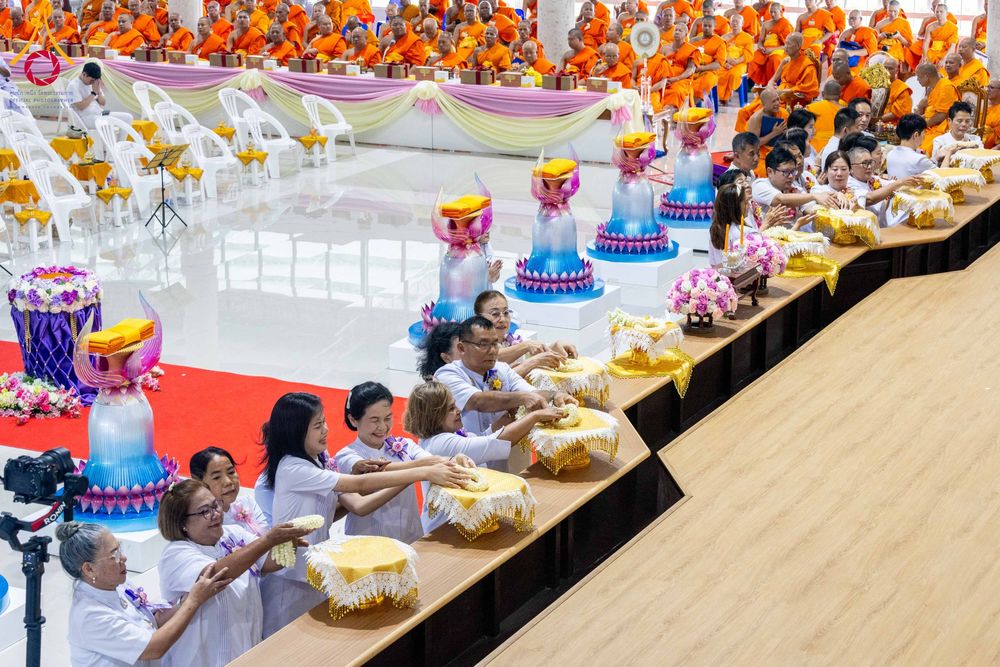 กลุ่มพุทธศาสนิกชนสวมชุดสีขาวกำลังประกอบพิธีบรรจุพระบรมสารีริกธาตุลงในเกศดอกบัวตูมจำลอง โดยมีพระภิกษุสงฆ์จำนวนมากนั่งอยู่ด้านหลัง