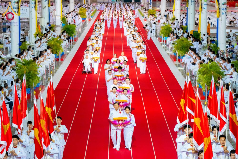 กลุ่มคนชุดขาวเดินแถวบนพรมแดงในอาคารขนาดใหญ่เพื่อประกอบพิธีทางศาสนา
