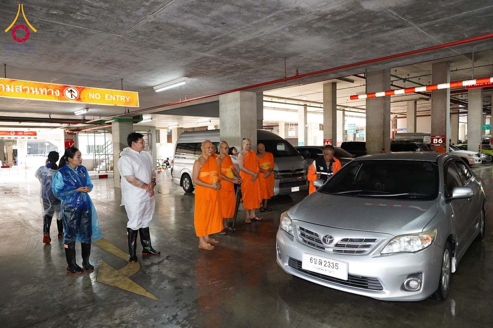 พระภิกษุสงฆ์และเจ้าหน้าที่ยืนรวมกลุ่มกันภายในอาคารจอดรถเพื่อตรวจดูความเรียบร้อย