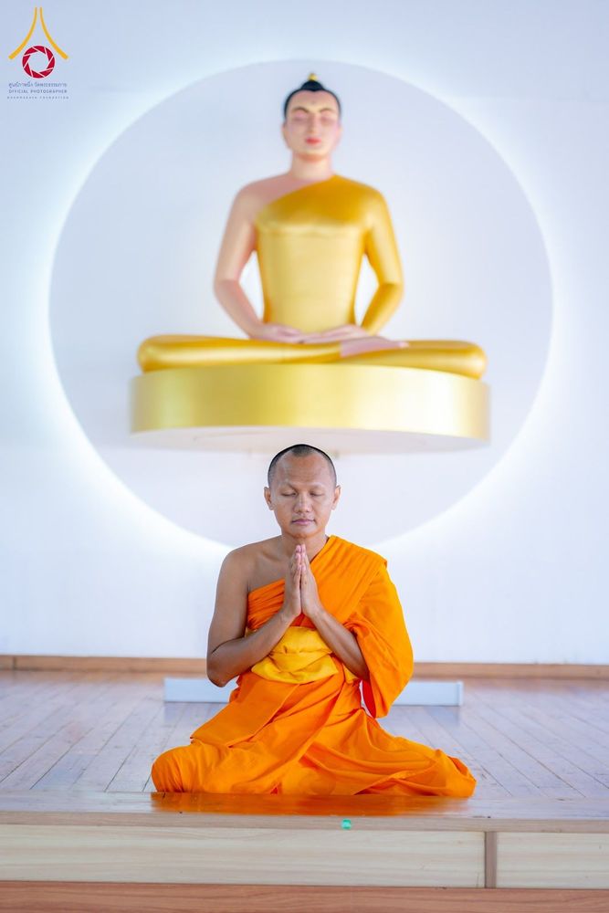 พระภิกษุสงฆ์นั่งสมาธิพนมมืออยู่หน้าพระพุทธรูปสีทอง