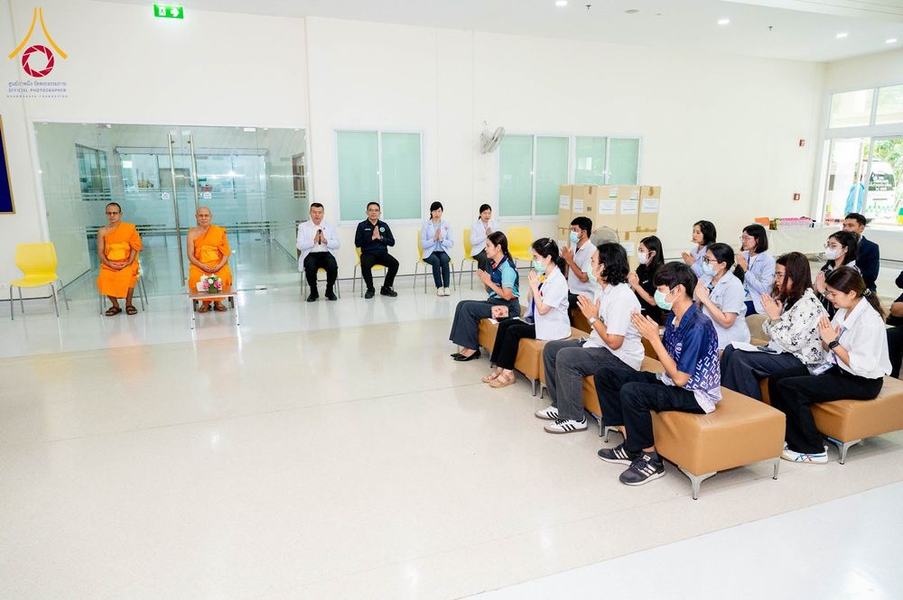 พระภิกษุสงฆ์และกลุ่มเจ้าหน้าที่สาธารณสุขนั่งในห้องโถงเพื่อร่วมพิธีมอบยา