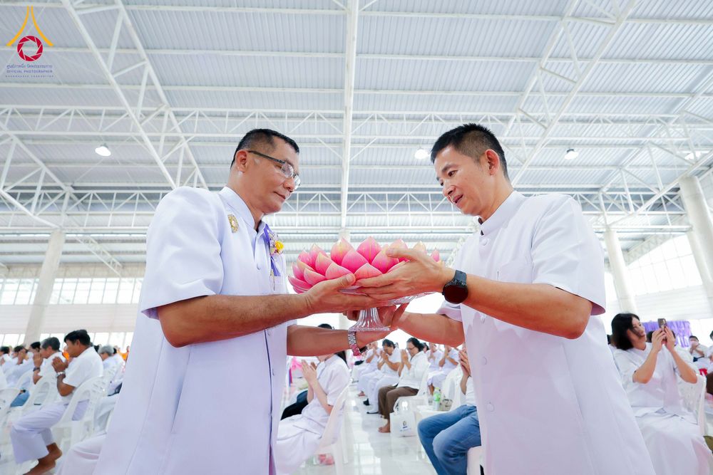 ชายสองคนสวมชุดสีขาวกำลังถือพานดอกบัวสีชมพูร่วมกันในพิธีทางศาสนา