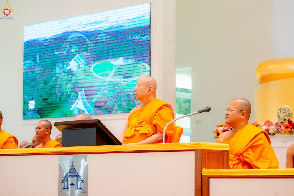 พระภิกษุสงฆ์หลายรูปนั่งอยู่บนเวทีในงานพิธีทางศาสนา โดยมีไมโครโฟนและจอภาพขนาดใหญ่เป็นฉากหลัง