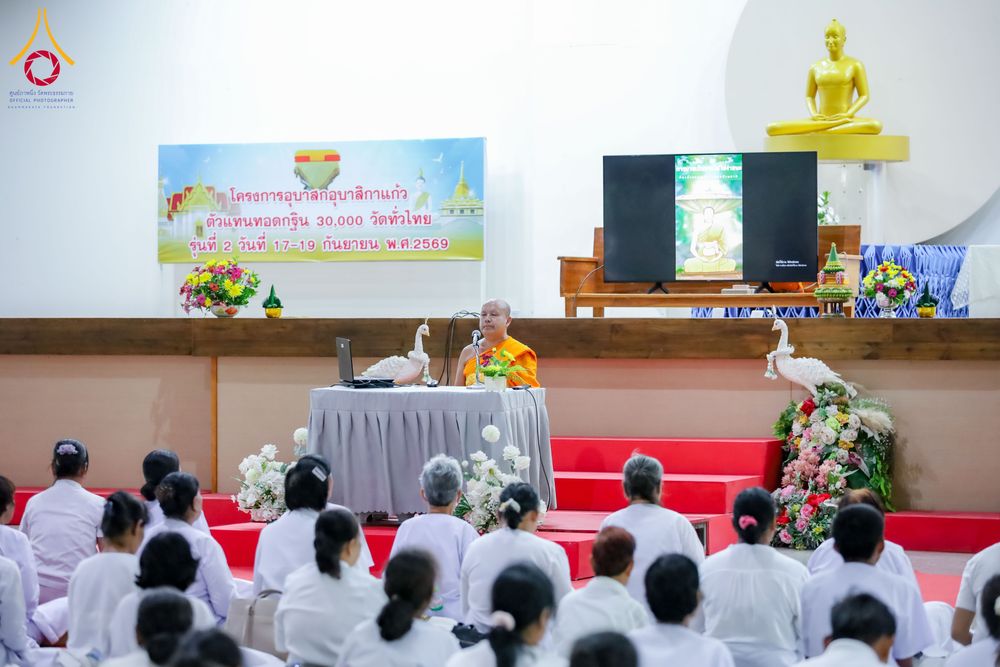 พระภิกษุสงฆ์นั่งบรรยายธรรมบนเวทีต่อหน้าผู้เข้าร่วมโครงการที่สวมชุดขาวจำนวนมาก