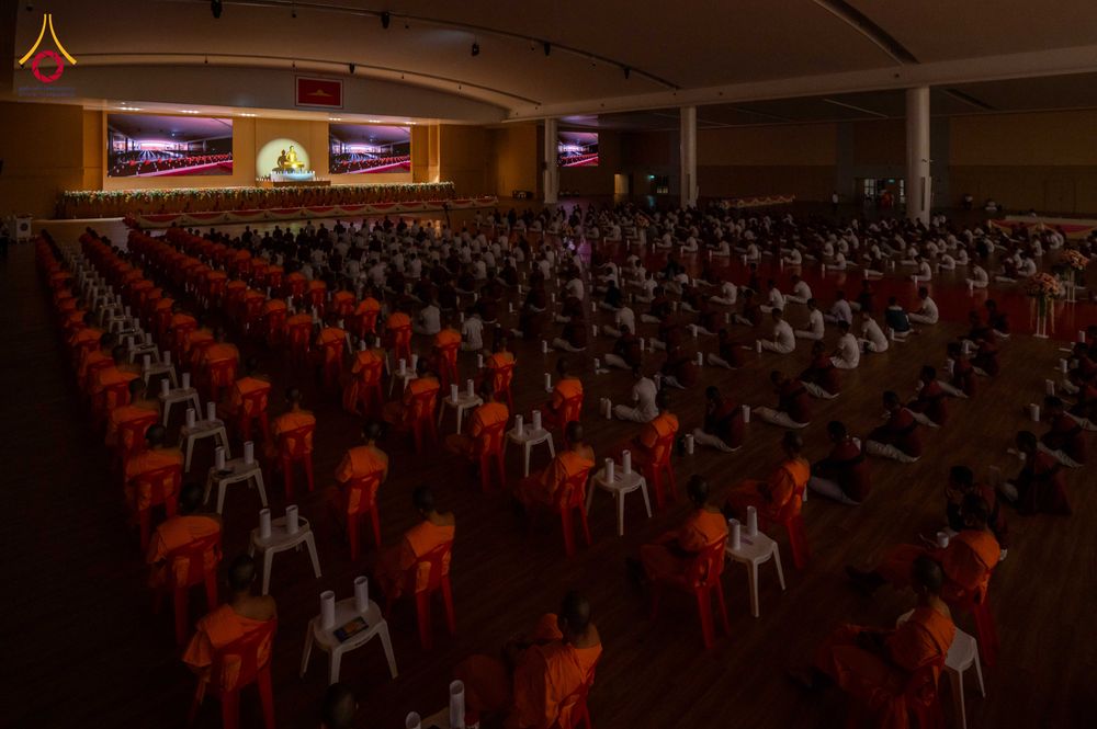 ผู้เข้าร่วมโครงการในชุดสีขาวและพระภิกษุนั่งปฏิบัติธรรมพร้อมเทียนในโถงกว้าง