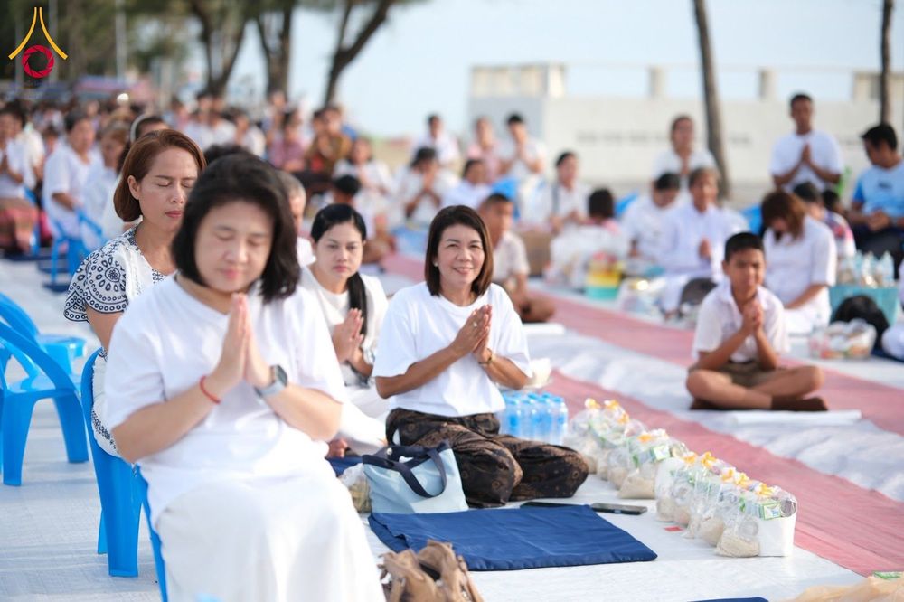 กลุ่มคนสวมชุดสีขาวนั่งพนมมือเตรียมตักบาตรริมชายหาด